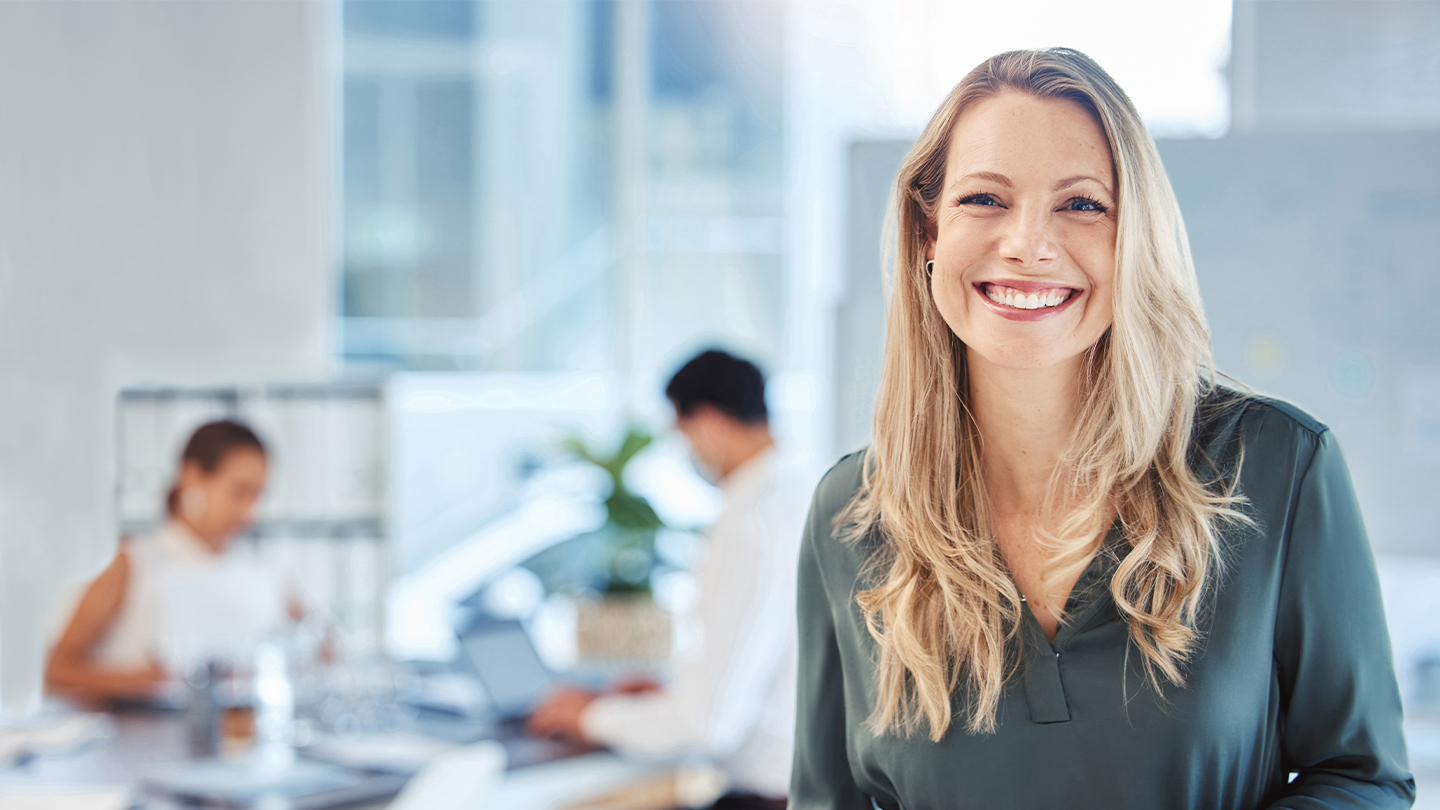 Frau lächelt freundlich im Office mit Mitarbeitenden im Hintergrund